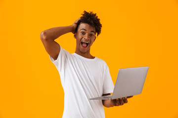 Excited young african man isolated over yellow background using laptop computer.