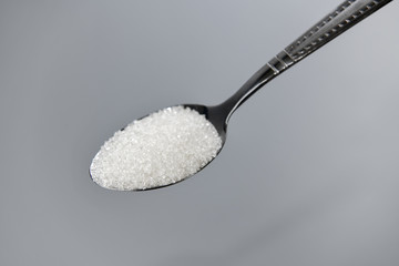 A spoonful of granulated sugar on gray background