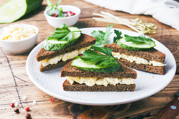 Sandwich with scrambled eggs, cucumbers and parsley on wooden rustic background.