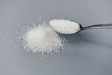 A spoonful of granulated sugar on gray background