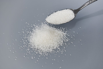 A spoonful of granulated sugar on gray background