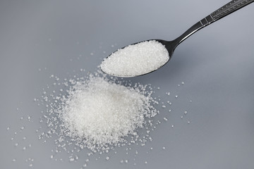 A spoonful of granulated sugar on gray background