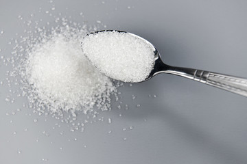 A spoonful of granulated sugar on gray background