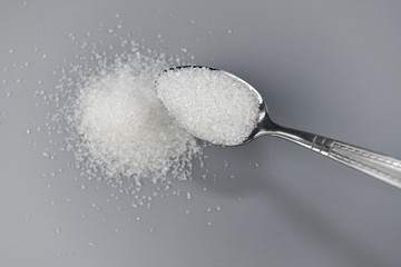 A spoonful of granulated sugar on gray background