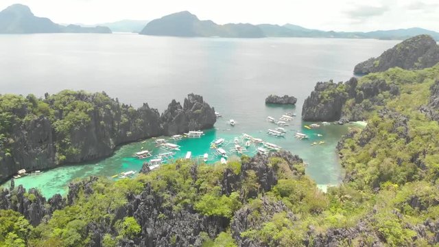 Aerial drone shot over a island, towards the ocean, revealing a turquoise lagoon, full of paraw boats, surrounded by limestone cliffs, on a sunny day, in the archipelago of Palawan, Philippines, Asia
