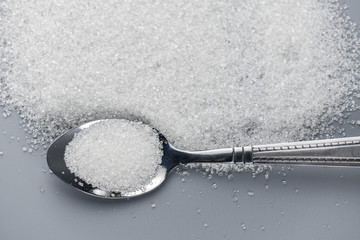 Fototapeta na wymiar A spoonful of granulated sugar on gray background
