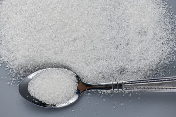 A spoonful of granulated sugar on gray background