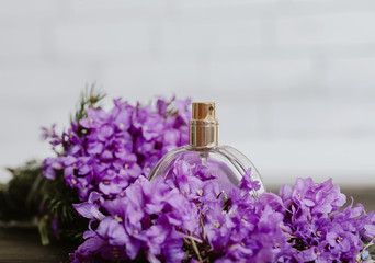 A jar of women's perfume stands near purple flowers