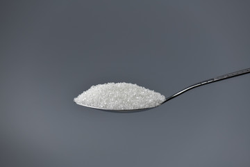A spoonful of granulated sugar on gray background
