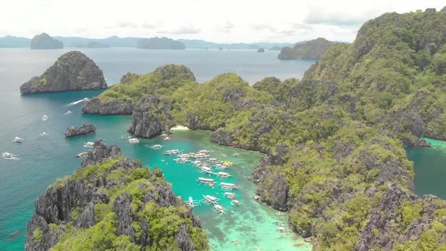 Aerial drone shot over limestone cliffs and towards a turquoise lagoon, full of Paraw boats, on a sunny day, on Palawan island, in Philippine archipelago, Philippines, Asia
