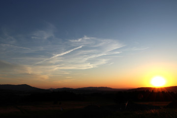 A beautiful sunset in czech lands with blue sky with small cloudies and dark land. Blue sky and dark meadows and incredible sun with sunshine
