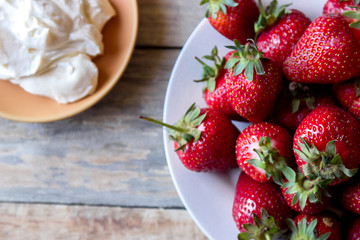 close-up top view of a strawberry in a plate and whipped cream in a saucer on a wooden table