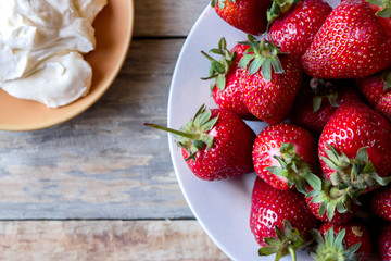 close-up view from above part of a plate with strawberries and saucers with whipped cream on a wooden table