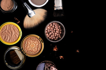 Set of bronze powder with makeup brushes on black background