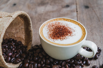 Coffee beans in the sack with a coffee cup on wooden table background.