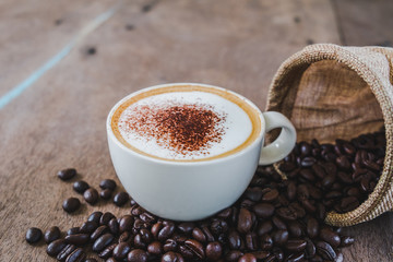Coffee beans in the sack with a coffee cup on wooden table background.