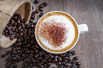 Coffee beans in the sack with a coffee cup on wooden table background.