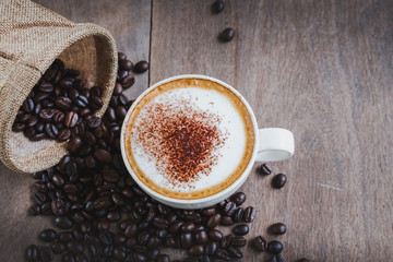 Coffee beans in the sack with a coffee cup on wooden table background.