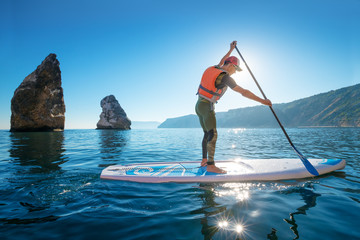 Young Man Having Fun Stand Up Paddling in the sea. SUP. Guy Training in the morning on Paddle Board...