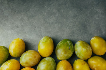 Pile of colorful freshly picked cherry plums on black grey stone background. Autumn fall harvest abundance concept. Poster with copy space