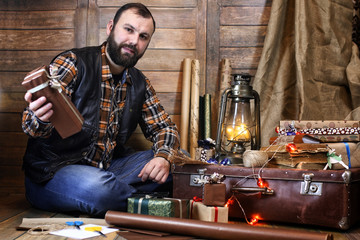 bearded man in shirt and vest packs Christmas gifts posing at ca