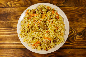 Pilaf with meat, rice, carrot and onion in a plate on wooden table. Top view