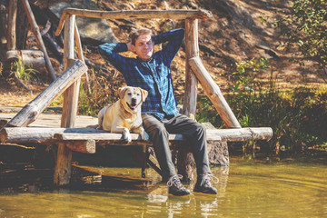 Fototapeta na wymiar The man with Labrador retriever dog sitting on the wooden deck on the lake shore. Man enjoying life