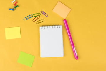Top view of blank notebook and school supplies like colored markers, sticker and clipers on yellow background. .