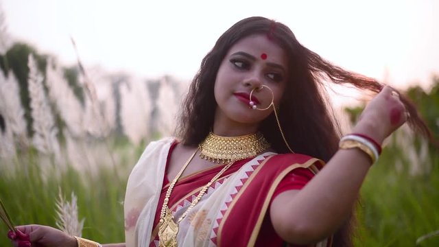 A newly wed cheerful and playful Indian woman plays with her beautiful curly long hair in a field outdoor at sunset or sunrise. Slow motion