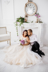 Wedding couple have a photo session in the amazing studio. Young couple hug and kiss while sitting...