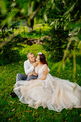 wedding, beautiful young bride lying together with groom in love on green grass kissing, park summer outdoor. Newlyweds wedding photoshoot.