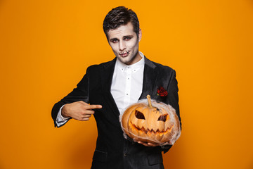 Photo of terrifying dead man on halloween wearing classical suit and creepy makeup holding carved...