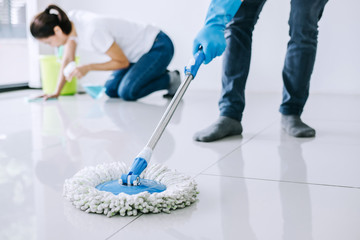 Housekeeping and cleaning concept, Young couple in blue rubber gloves wiping dust using mop and duster while helping cleaning on floor at home
