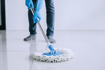 Husband housekeeping and cleaning concept, Happy young man in blue rubber gloves wiping dust using mop while cleaning on floor at home - obrazy, fototapety, plakaty