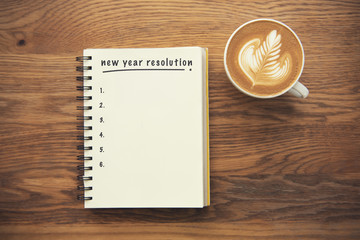 Coffee cup and notebook with new years resolution on rustic desk from above, planner and checklist...