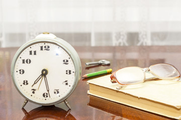 old metal alarm clock, glasses, book on the old table