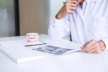 Male doctor or dentist writing report working with tooth x-ray film, model and equipment used in the treatment of dental and dentistry at workplace