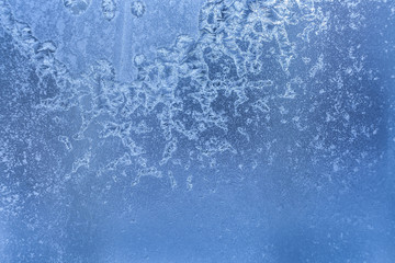 Blue frozen winter glass pane with bizarre frosty pattern of ice crystals.