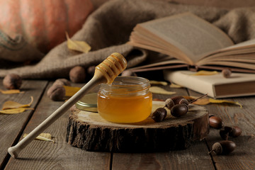 Autumn composition with honey close-up and acorns on a wooden stand on a brown wooden table