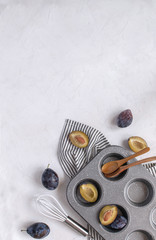 Autumn baking concept - Fresh plums, Cupcake metal mold, Whisk, wooden spoons, vanilla bean on Crumpled Striped Napkin.