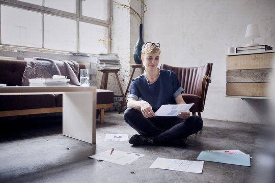 Smiling woman sitting on the floor in a loft looking at papers
