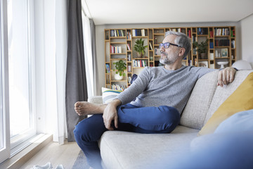 Mature man relaxing on couch in his living room looking out of window