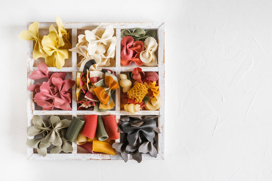Mixed set of dry multi-colored Italian pasta on a white old wooden box. Background. Close up.