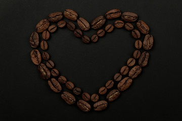 Roasted coffee beans placed in a shape of heart on black background