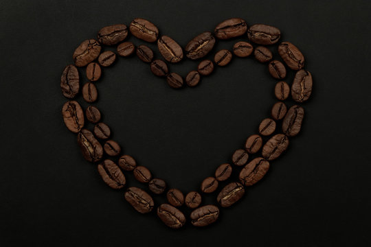 Roasted coffee beans placed in a shape of heart on black background