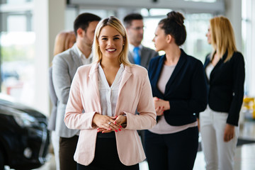 Group of happy car sales consultants working inside vehicle showroom