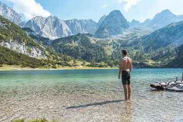 Austria, Tyrol, Young man at Lake Seebensee standing ankle deep in water