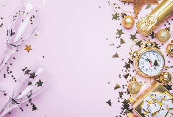 Christmas or New Year composition, frame, pink background with gold Christmas decorations, stars, snowflakes, balls, alarm clock, gift box and bottle of champagne, top view