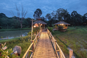 Wooden pathway bridge with thatch cottage illumination