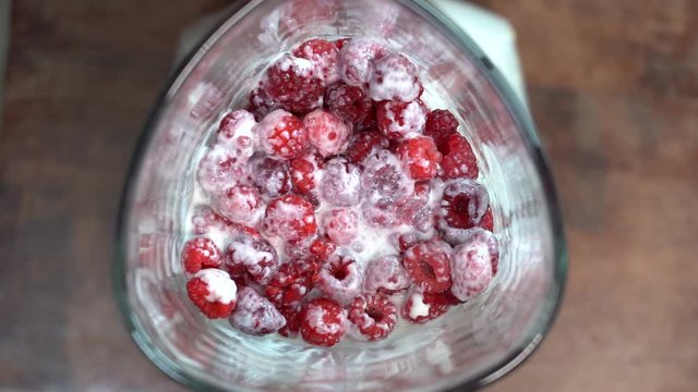 Smoothie blended in slow motion shot from above using fruit raspberries and yoghurt. Raw red raspberry mixing into blender. Healthy eating, food, dieting and vegetarian concept. Crimson smoothies